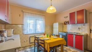 A kitchen with a dining table set for four, a refrigerator, and a stove. - Apartment Eugen (Crikvenica)