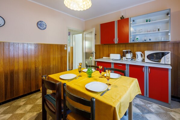 A dining area with a yellow table set for four, wooden paneling on the walls, a red cabinet with glass shelves above, and a microwave on the counter.