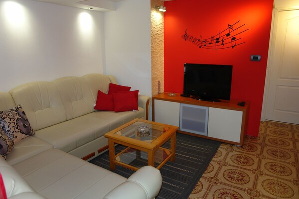 Una sala de estar con un sofá, una mesa de centro, una televisión y una pared de acento roja.
