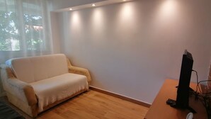 Una sala de estar con un sofá, un televisor de pantalla plana sobre una mesa de madera y una ventana con persianas.