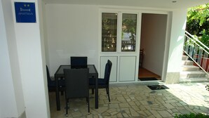 Un pequeño espacio exterior con una mesa y sillas, un cartel que indica que es un apartamento, y una escalera que sube a un nivel superior.