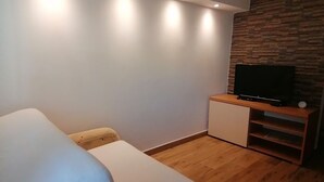 Un dormitorio moderno con una cama, un televisor sobre un soporte de madera e iluminación empotrada.