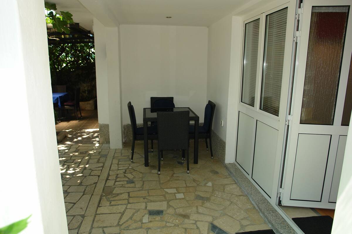 A covered patio area with a stone floor, a table with chairs, and a door with a window.