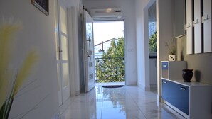 A hallway with a glossy tiled floor, a white door leading outside, and a small balcony with a view of greenery. - Apartment Novakovic (Crikvenica)