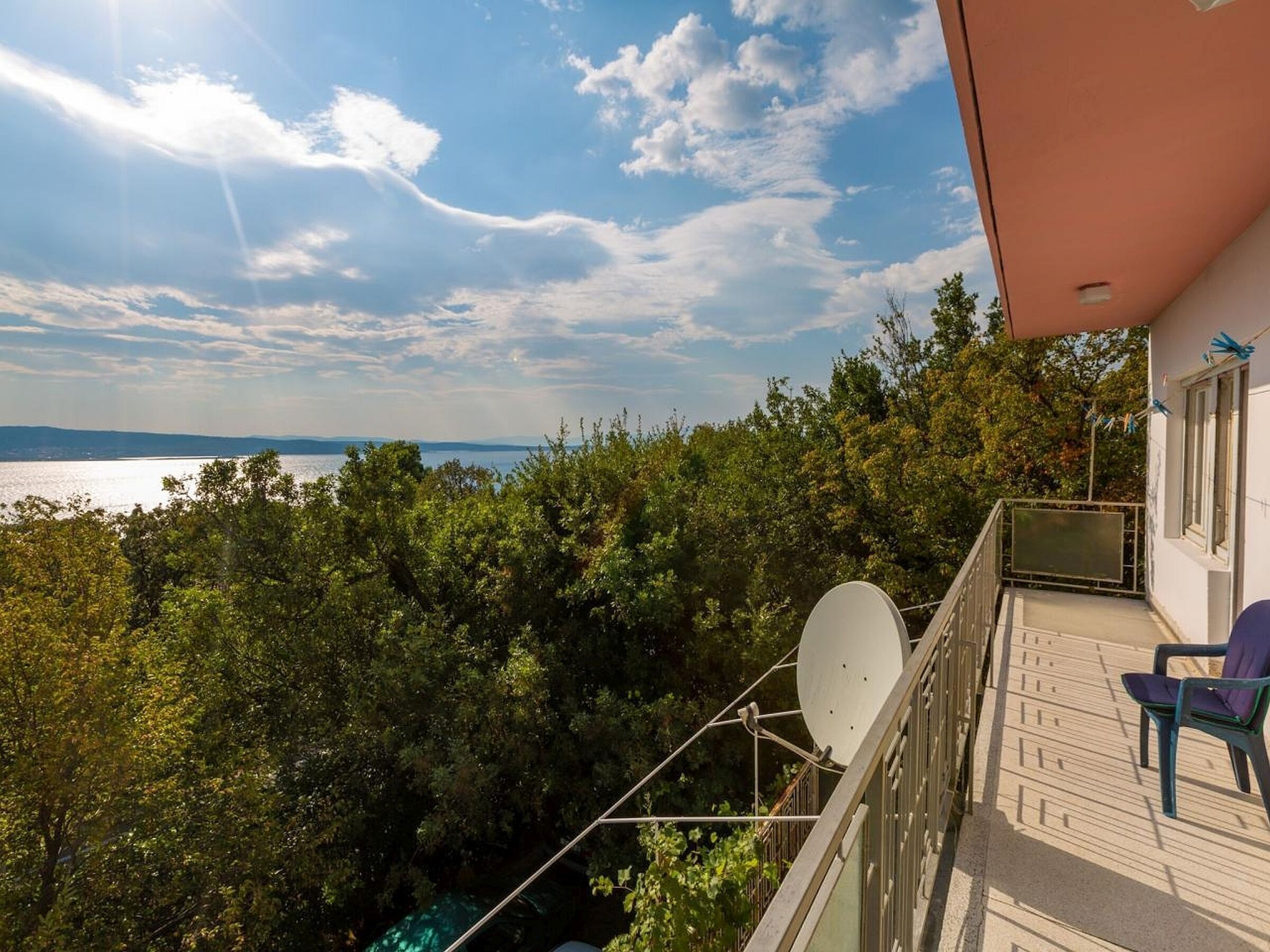 Een balkon met uitzicht op een meer, omgeven door bomen, en een schotelantenne.