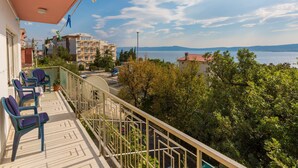 A balcony with chairs, a view of a body of water, and buildings in the background. - Apartment Novakovic (Crikvenica)