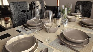A dining table set with plates, glasses, and a bottle of wine, surrounded by patterned chairs. - Apartment Novakovic (Crikvenica)