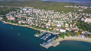 An aerial view of a coastal town with a marina, residential buildings, and a hilly backdrop. - Apartment Suzy (Dramalj)