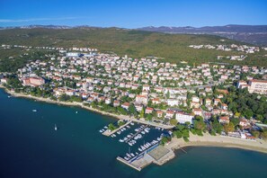 Vue aĂ©rienne dâune ville cĂŽtiĂšre avec un port de plaisance, des immeubles rĂ©sidentiels et une chaĂźne de collines en arriĂšre-plan.
