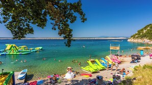 Uma praia com águas cristalinas, pessoas nadando e botes infláveis coloridos.