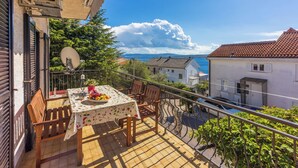 A balcony with a table set for two, overlooking a coastal area with buildings and a clear sky. - Apartment Suzy (Dramalj)