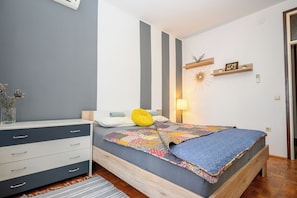 Ein Schlafzimmer mit Bett, Nachttisch, Kommode, Lampe und Wandregal mit Dekoration.