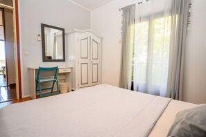 A bedroom with a bed, a chair, a wardrobe, a mirror, and a window with curtains.