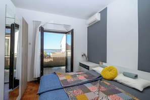 A bedroom with a bed, a bedside table, a nightstand, a window with curtains, and an air conditioning unit. - Apartment Suzy (Dramalj)