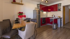 Eine moderne Küche mit roten Schränken, einem Edelstahlkühlschrank und einer Essecke mit Holztisch und Stühlen.