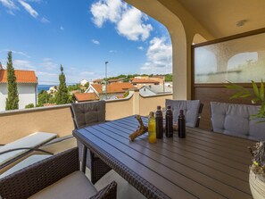 A terrace with wicker furniture, a table, and bottles, overlooking a residential area with red-tiled roofs. - Apartments Ninac (Klenovica)