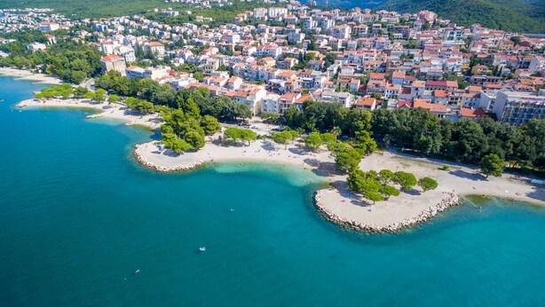 Vista aerea di una località balneare con spiaggia, acque blu cristalline e edifici affollati.