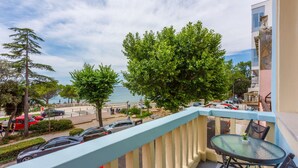 Un balcone con vista sul mare, un tavolo con sedie e auto parcheggiate.