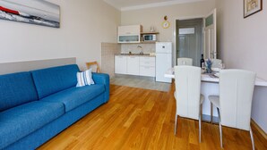 Un soggiorno moderno con un divano blu, un'area pranzo con sedie bianche, una cucina con mobili bianchi e un forno a microonde.