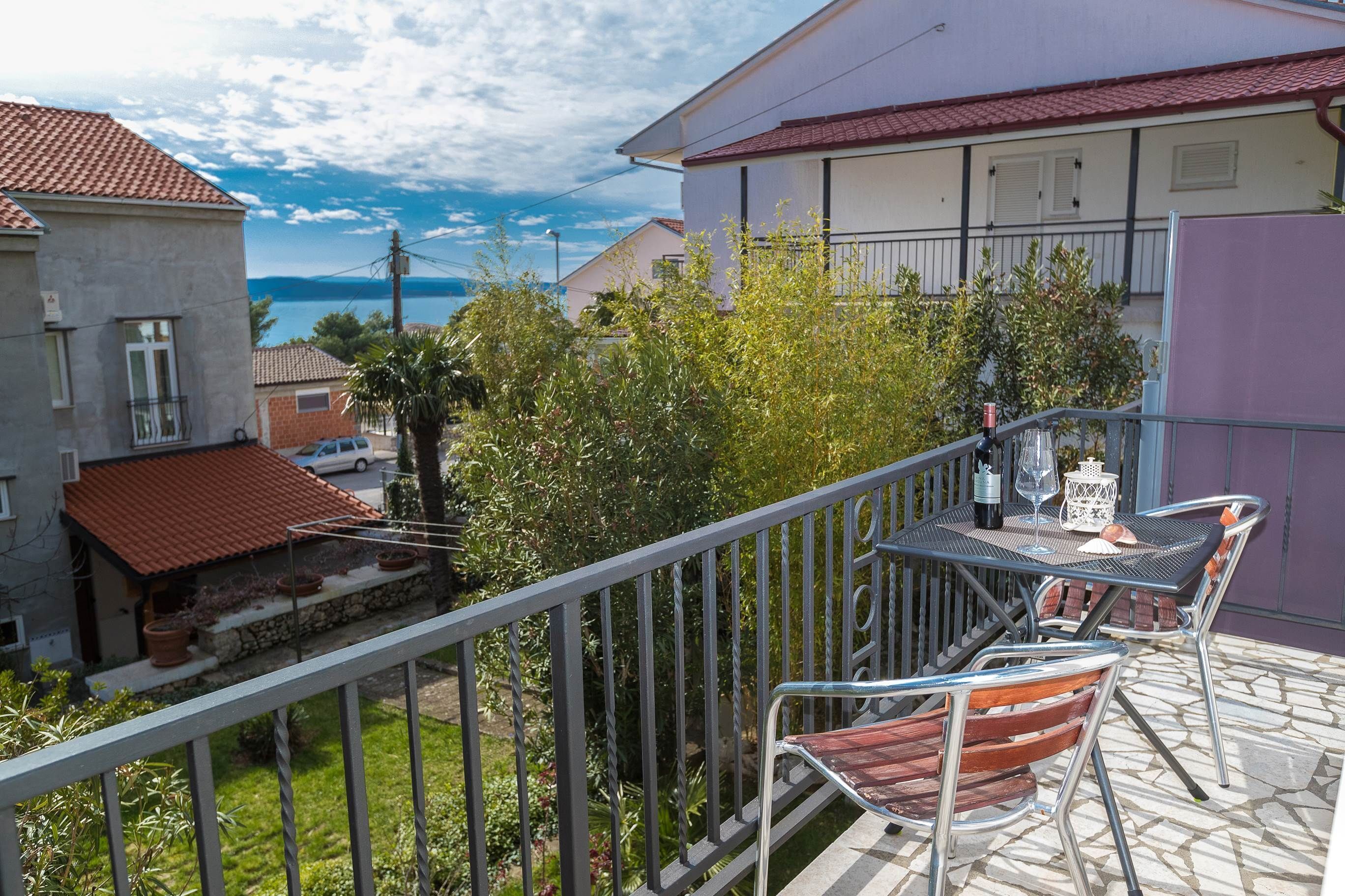 A balcony with a table and chairs, overlooking a garden and a view of the sea.