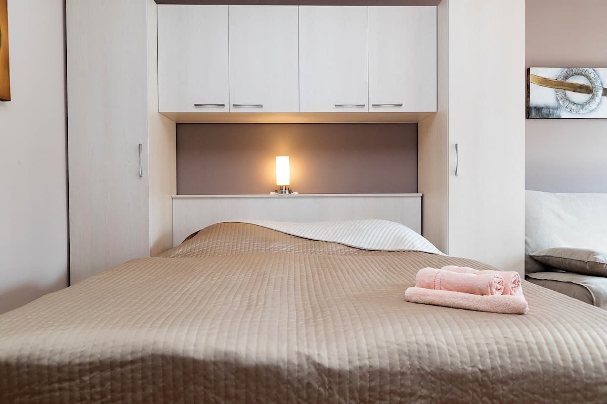 A neatly made bed with a beige quilt, a bedside lamp, and a folded towel on the bed.