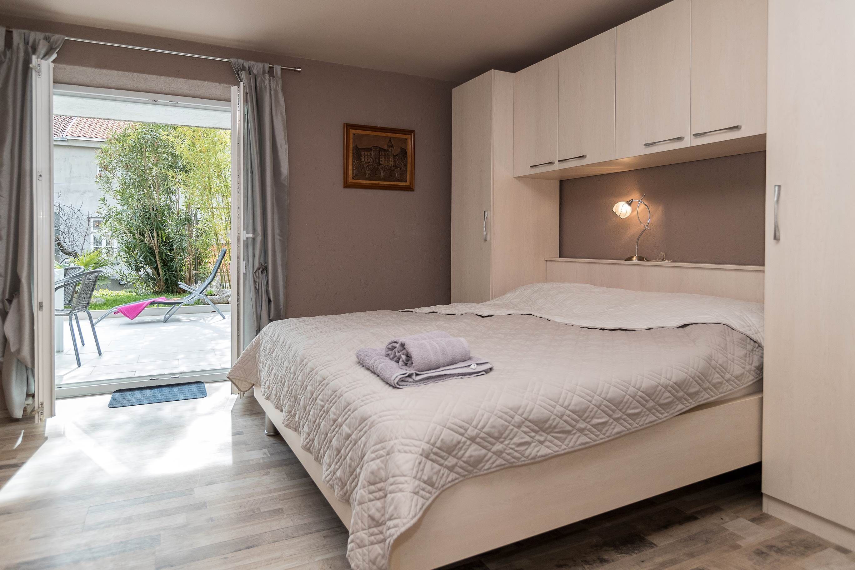 A bedroom with a bed, a bedside table with a lamp, a window with curtains, and a view of the outside.
