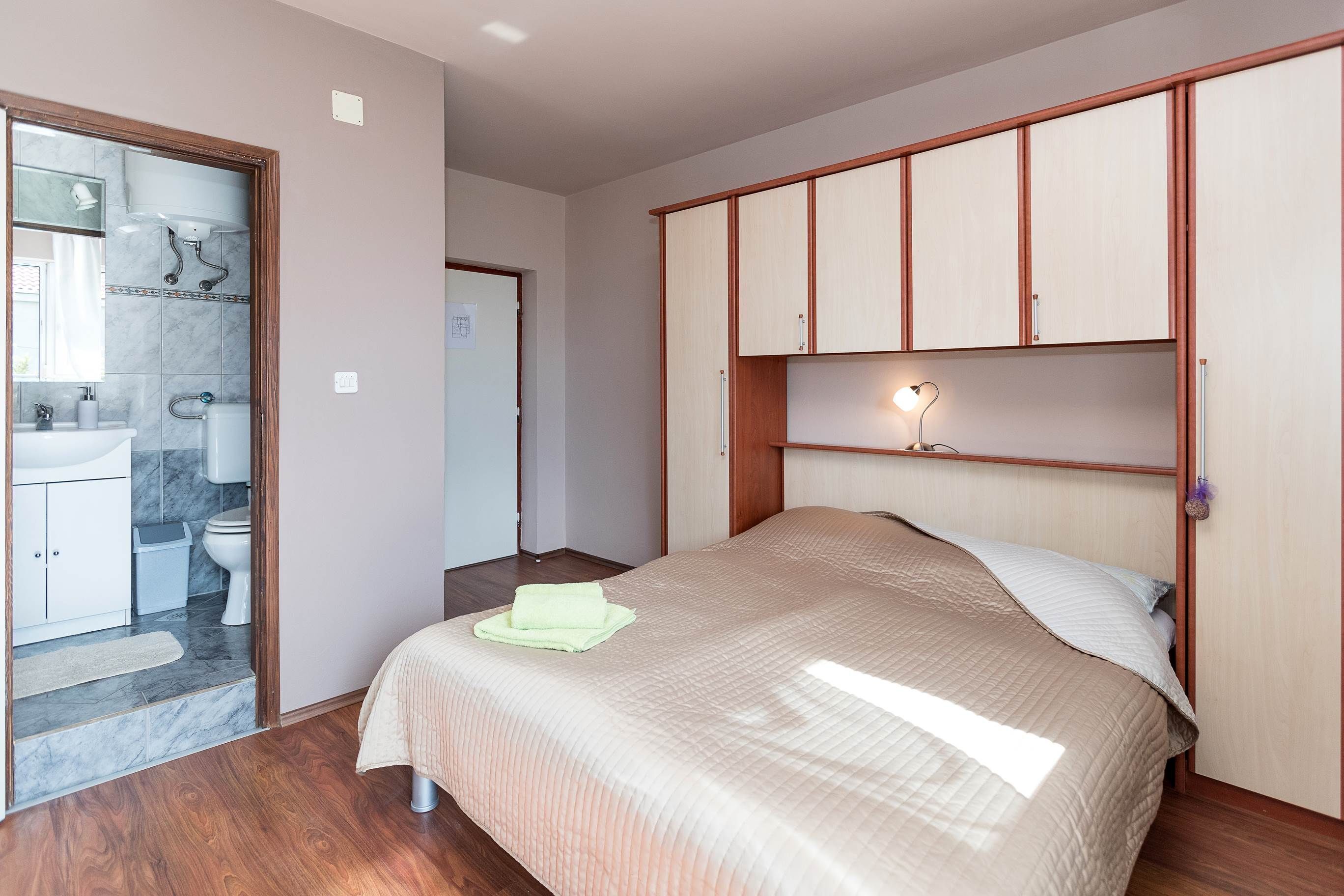 Ein Schlafzimmer mit Bett, Holzschrank und einem Badezimmer mit Waschbecken und Toilette.