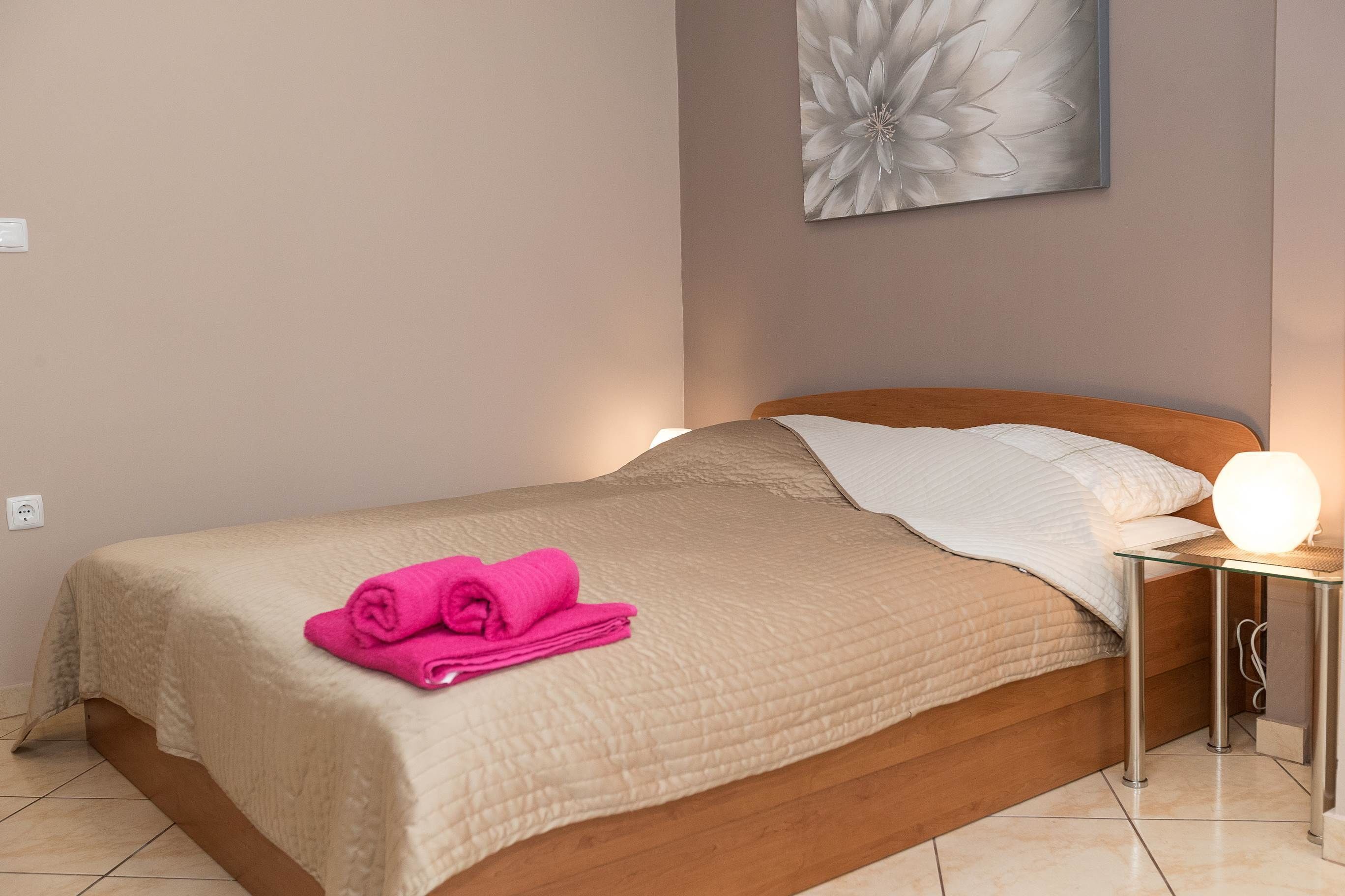 A neatly made bed with a beige quilt, a pink towel, and a bedside lamp.