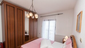 A bedroom with a bed, wooden wardrobe, and a hanging light fixture. - Apartment Marinko (Crikvenica)