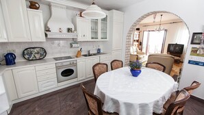 A kitchen with white cabinets, a sink, and a dining area with a table and chairs. - Apartment Marinko (Crikvenica)