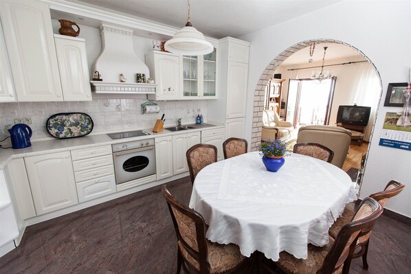 A kitchen with white cabinets, a sink, and a dining area with a table and chairs. - Apartment Marko (Crikvenica)