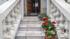 A staircase leading to a wooden door with a white railing and potted plants. - Apartment Marinko (Crikvenica)
