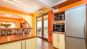 Una cocina moderna equipada con microondas, horno y refrigerador integrados. Cuenta con un comedor con mesa y sillas, y vista al exterior a través de una puerta de vidrio.