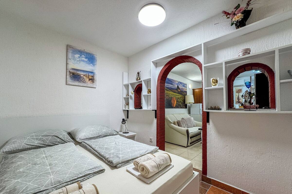 A bedroom with a bed, a nightstand, a lamp, a sofa, and a mirror.