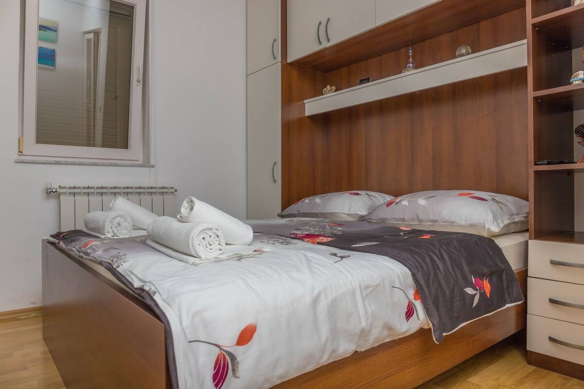 A bedroom with a bed, a wooden wardrobe, a radiator, and a window.