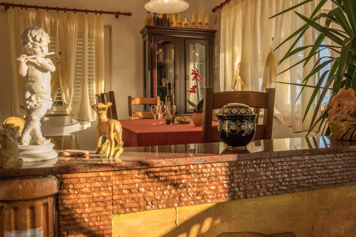 A dining area with a table set for two, a cabinet with glass doors, and a statue of a cherub.