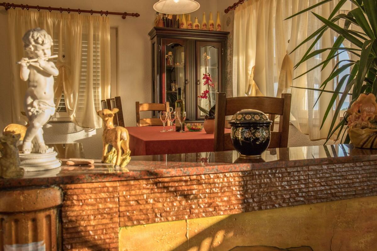 A dining area with a table set for two, a cabinet with glass doors, and a statue of a cherub.
