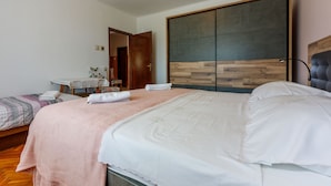 Ein Schlafzimmer mit einem großen Bett, einem kleineren Bett, einem Kleiderschrank, einem Schreibtisch und einem Stuhl.