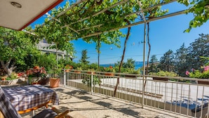 Ein Balkon mit Tisch und Stühlen, Blumentöpfen und Blick auf die Straße und die Berge.