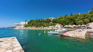 A coastal town with a stone pier, boats, and a beach area with umbrellas and people. - Apartment Kompes (Dramalj)