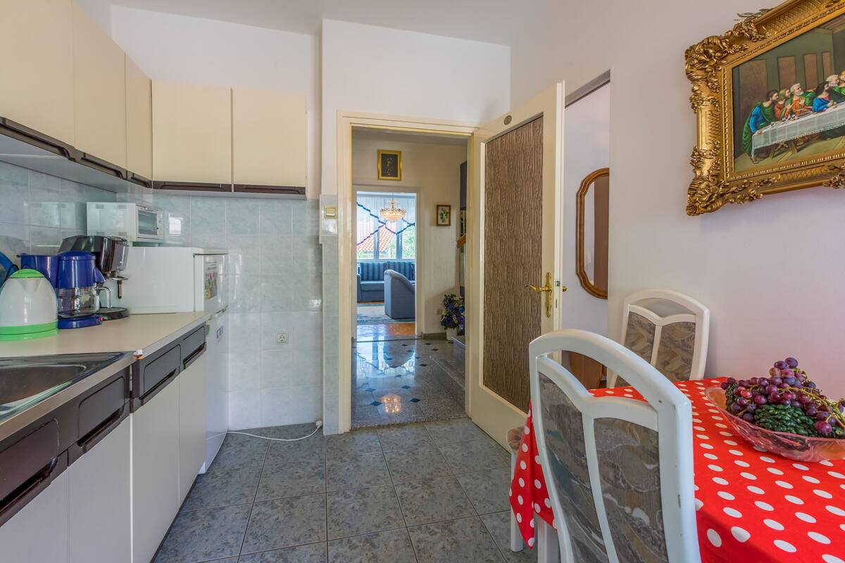 Una cocina con armarios blancos, un microondas y una cafetera. Hay un comedor con una mesa cubierta con un mantel rojo de lunares y un tazón de uvas.