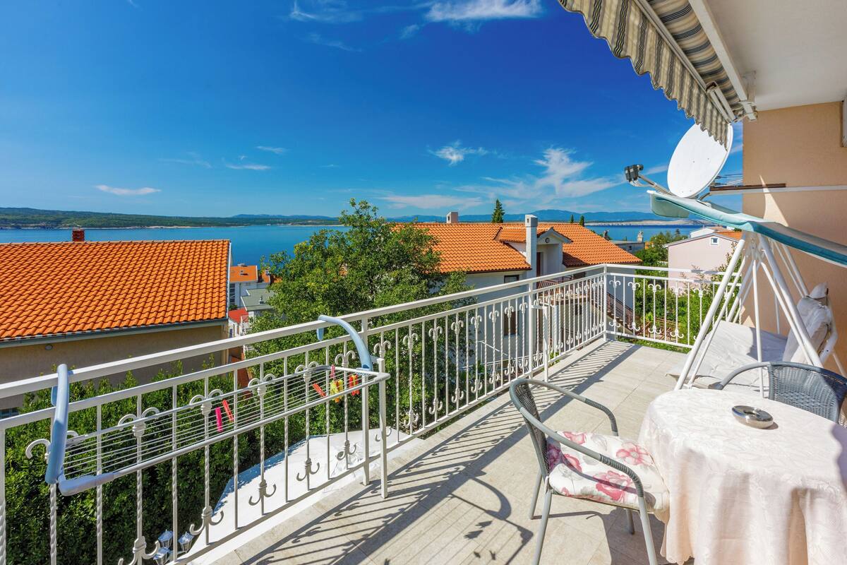 A balcony with a view of the sea, a table with a chair, and a satellite dish.