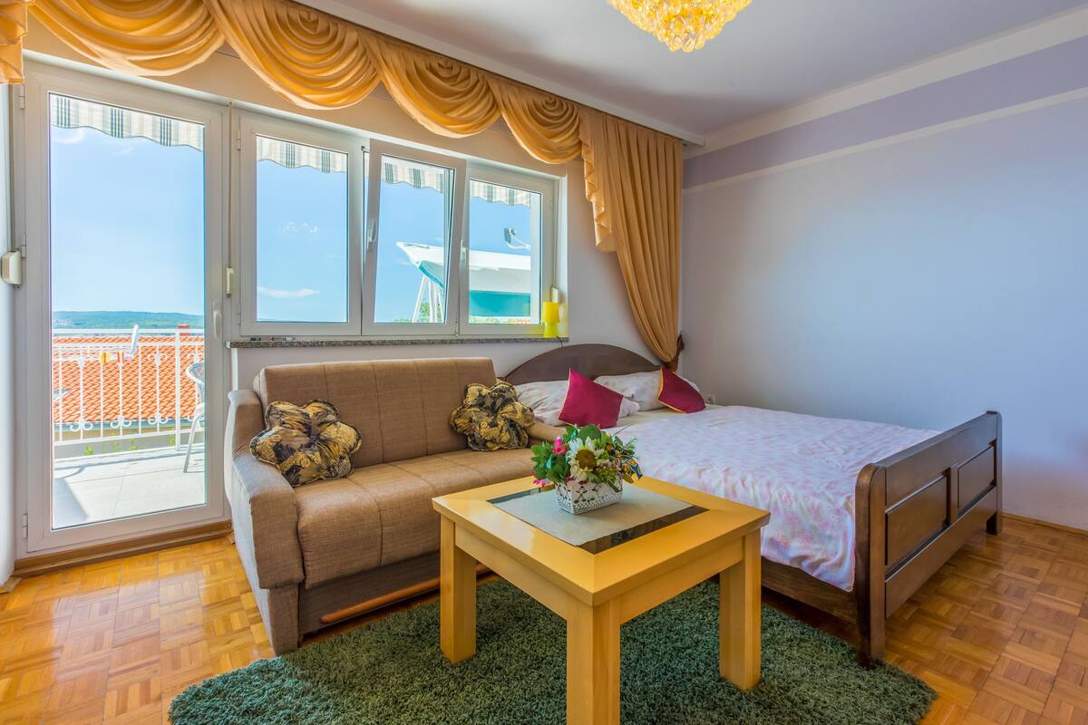 Un dormitorio con cama, sofá, una mesita y vistas al balcón exterior.