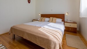 Un lit bien fait, avec une tête de lit en bois, deux tables de chevet avec des lampes, un petit objet décoratif accroché au mur et un plancher en bois.