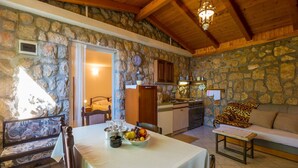 A cozy room with a stone wall, wooden ceiling, a dining table with a fruit bowl, a sofa, and a kitchen area with a stove and cabinets. - Apartments Stipe (Novi Vinodolski)