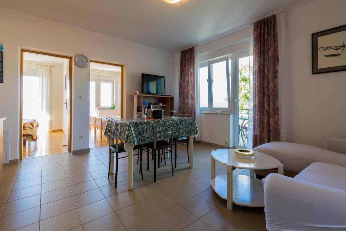 A living room with a sofa, a dining table with chairs, a TV, and a window with curtains.