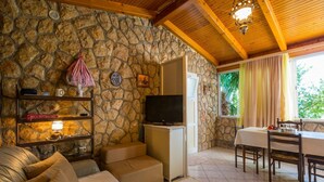 A cozy living room with stone walls, a television, a sofa, and a dining area with a table and chairs. - Apartments Stipe (Novi Vinodolski)