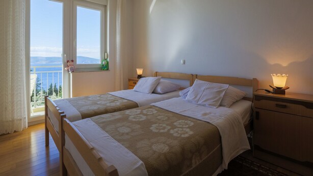 A double room with two beds, a nightstand, and a window with a view of the sea. - Apartments Stipe (Novi Vinodolski)