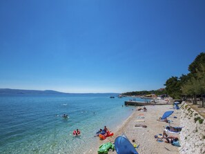 Una playa con agua cristalina, gente nadando y tomando el sol, y un litoral rocoso.