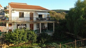 Une maison à deux étages, avec un toit en tuiles, un balcon et un jardin.
